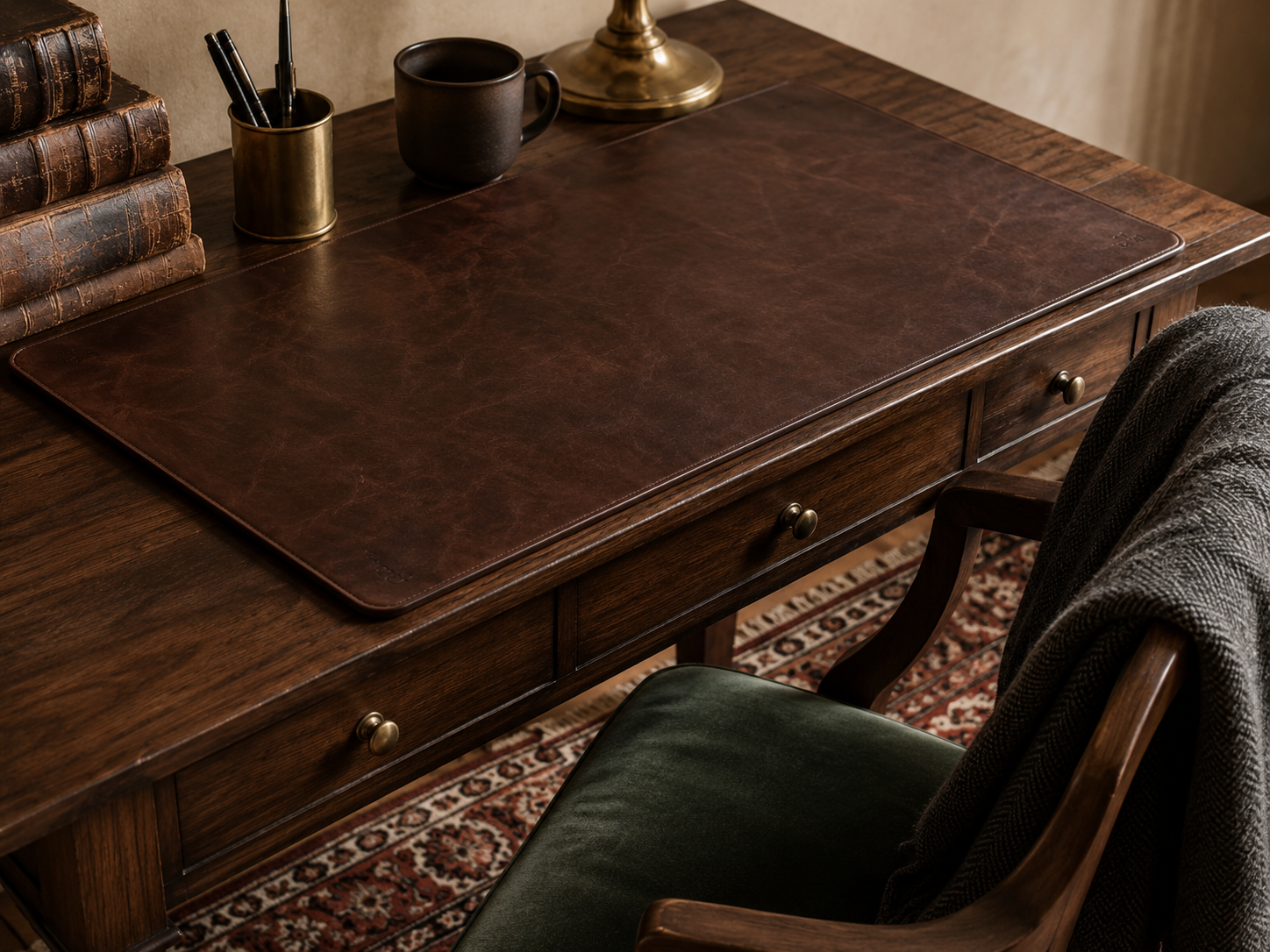 A dark academia workspace layering oxblood leather, forest green velvet, charcoal wool, and Persian rug textures across desk and chair