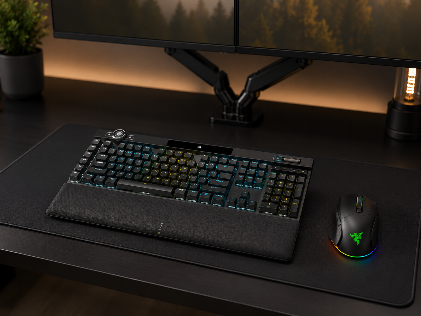 A mechanical keyboard and gaming mouse on a desk mat beneath a dual monitor setup