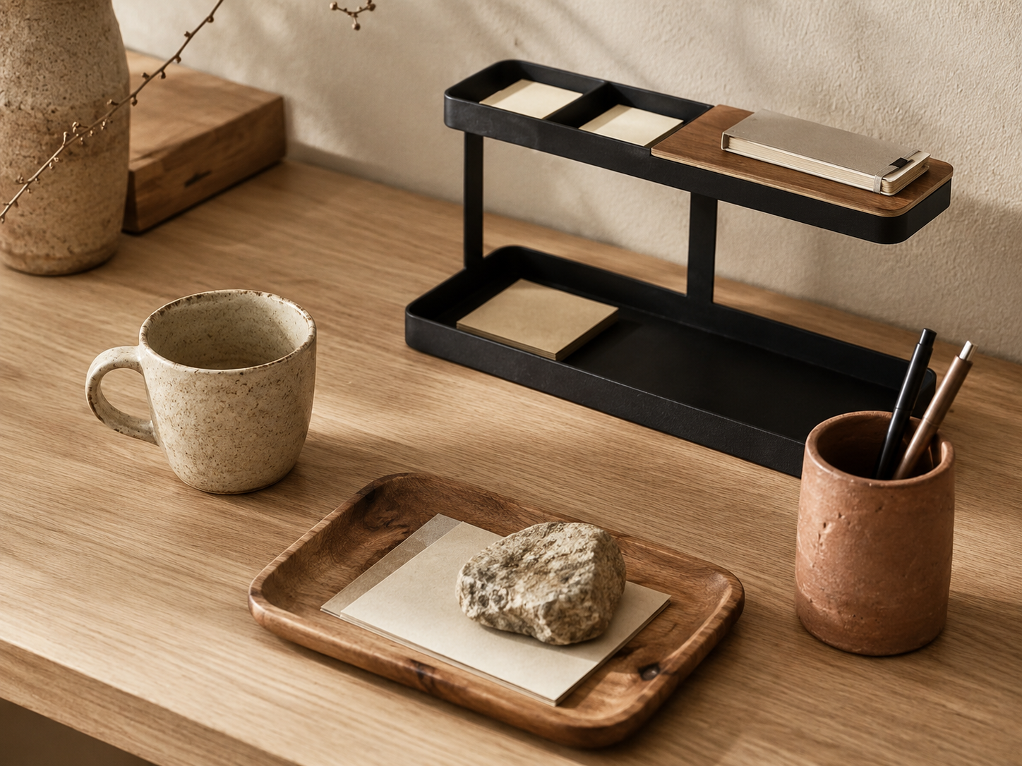 A Japandi desk featuring handmade ceramic vessels with visible throwing marks, a stoneware mug, and a wooden tray with grain irregularities alongside a minimalist matte desk organizer