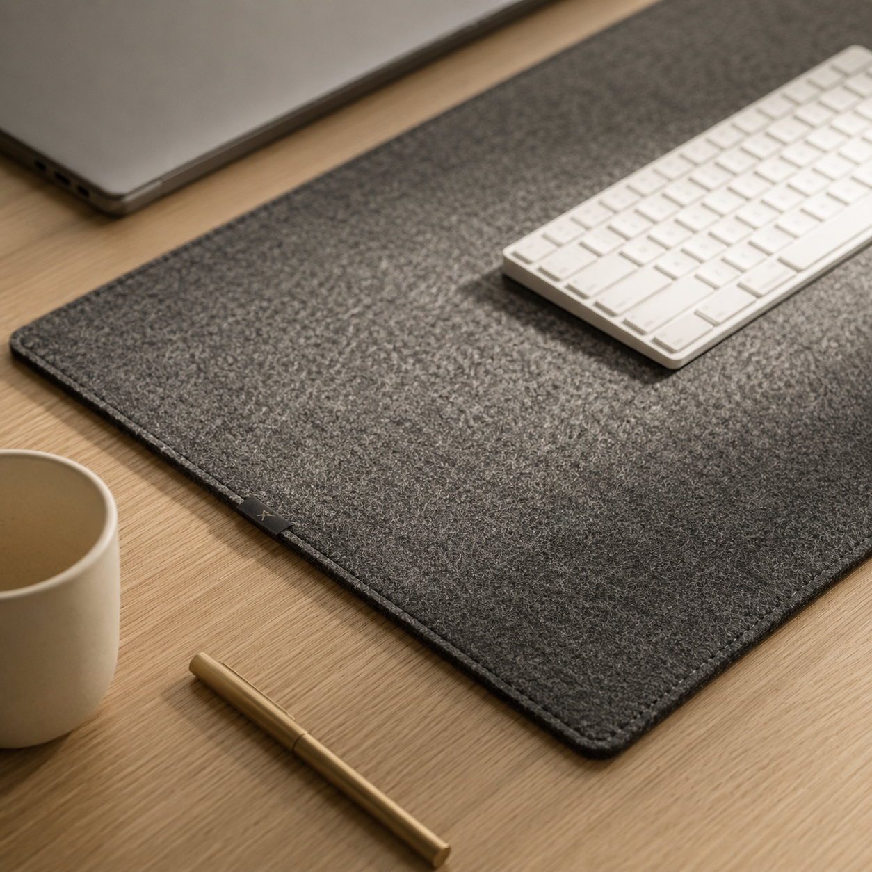 Grovemade wool felt desk pad in warm gray with visible woven texture and stitched edges on a white oak desk