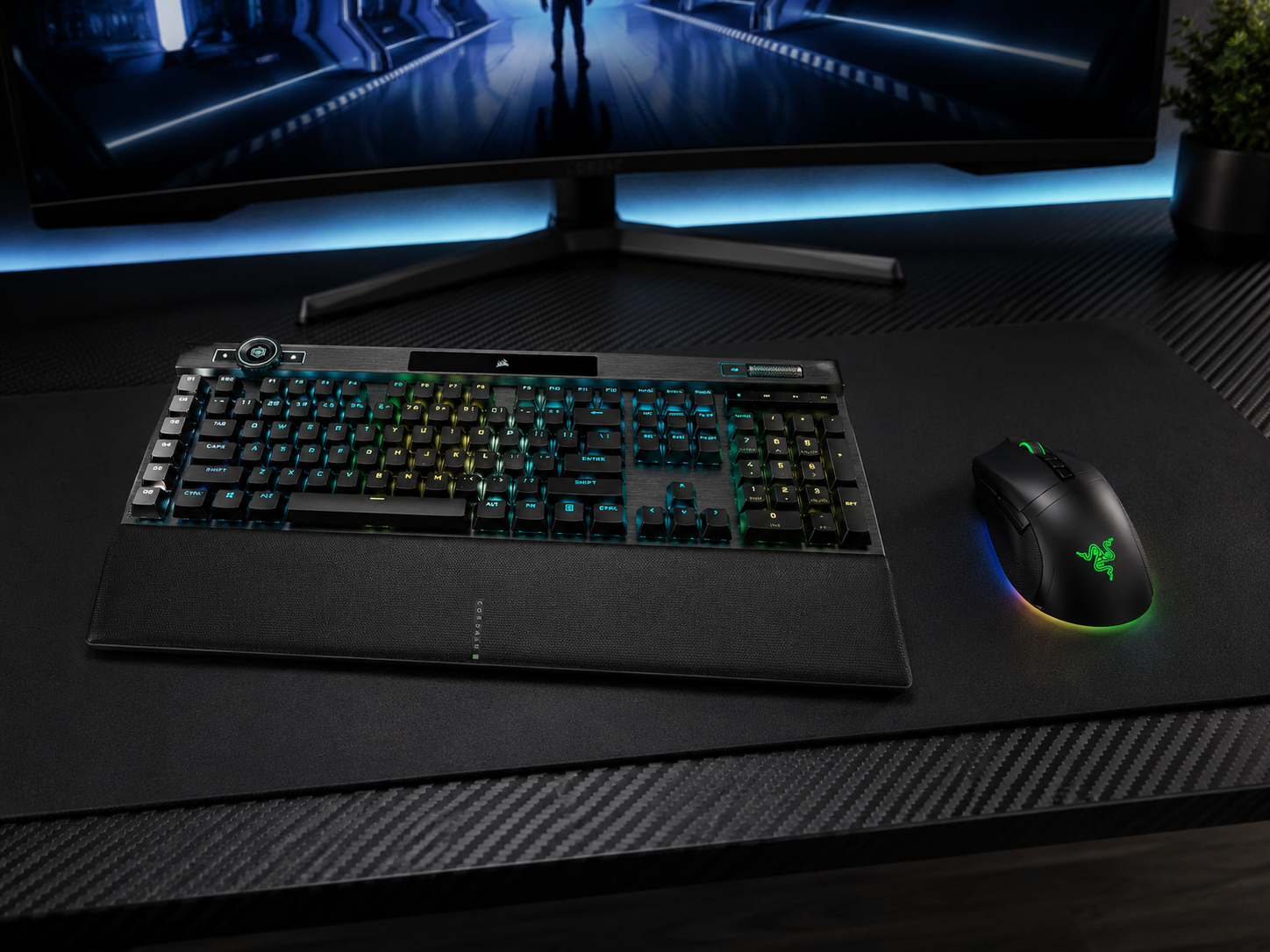 A mechanical keyboard and gaming mouse in a restrained dark colorway on a desk mat beneath a curved ultrawide