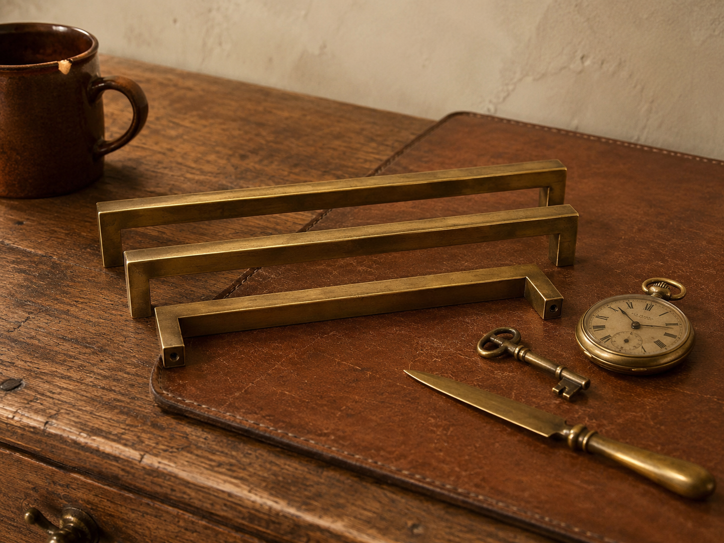 Close-up of aged brass drawer pulls, worn cognac leather desk pad, and weathered oak grain showing authentic patina on multiple vintage materials